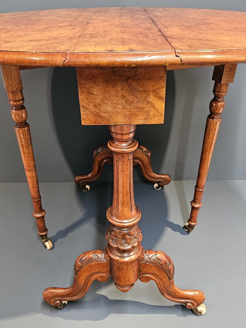 A Victorian burr walnut baby Sutherland table featuring two drop leaves, dual turned column supports, and carved feet on white ceramic castors. View VIII