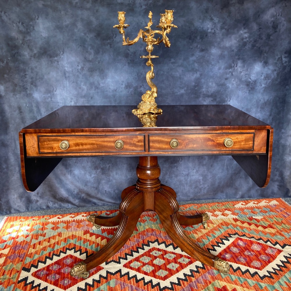 A Regency mahogany sofa table featuring two drop-leaf ends, twin frieze drawers with brass handles, ebony inlay, and reeded sabre legs with brass paw castors. View III