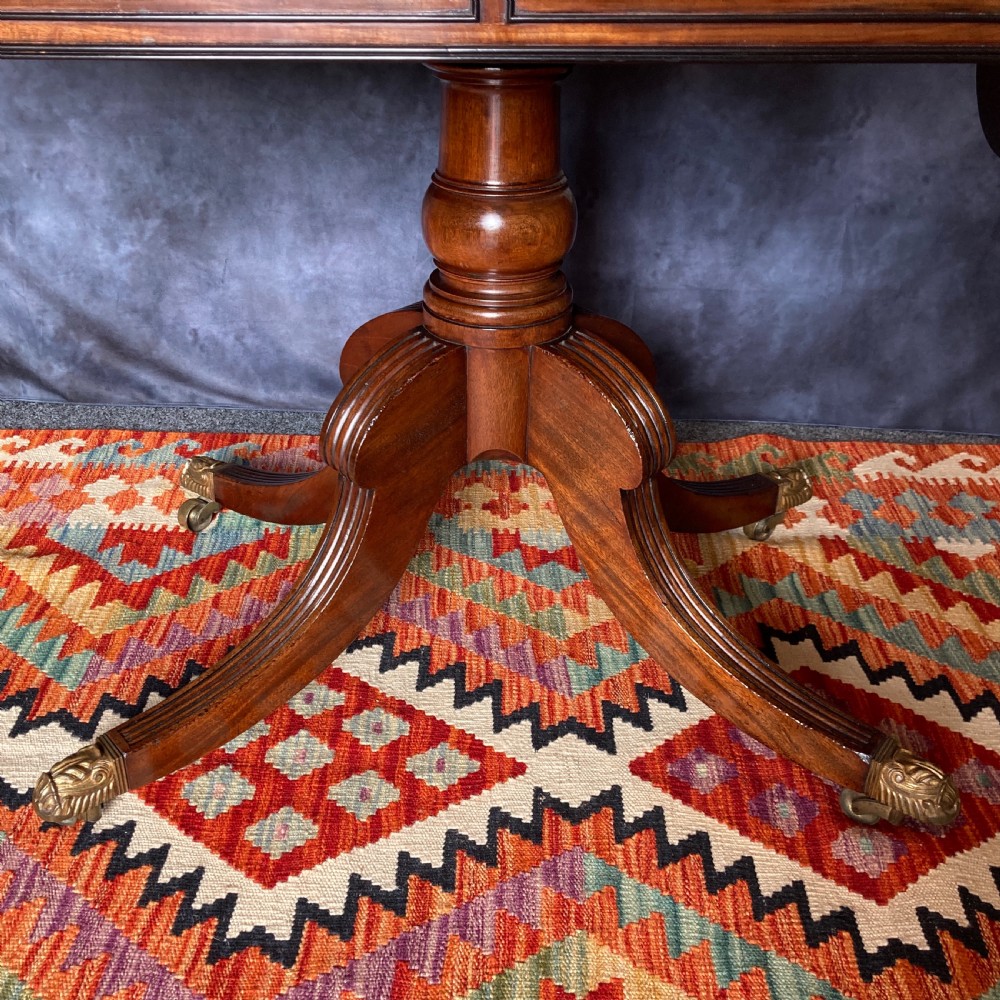 A Regency mahogany sofa table featuring two drop-leaf ends, twin frieze drawers with brass handles, ebony inlay, and reeded sabre legs with brass paw castors. View IX