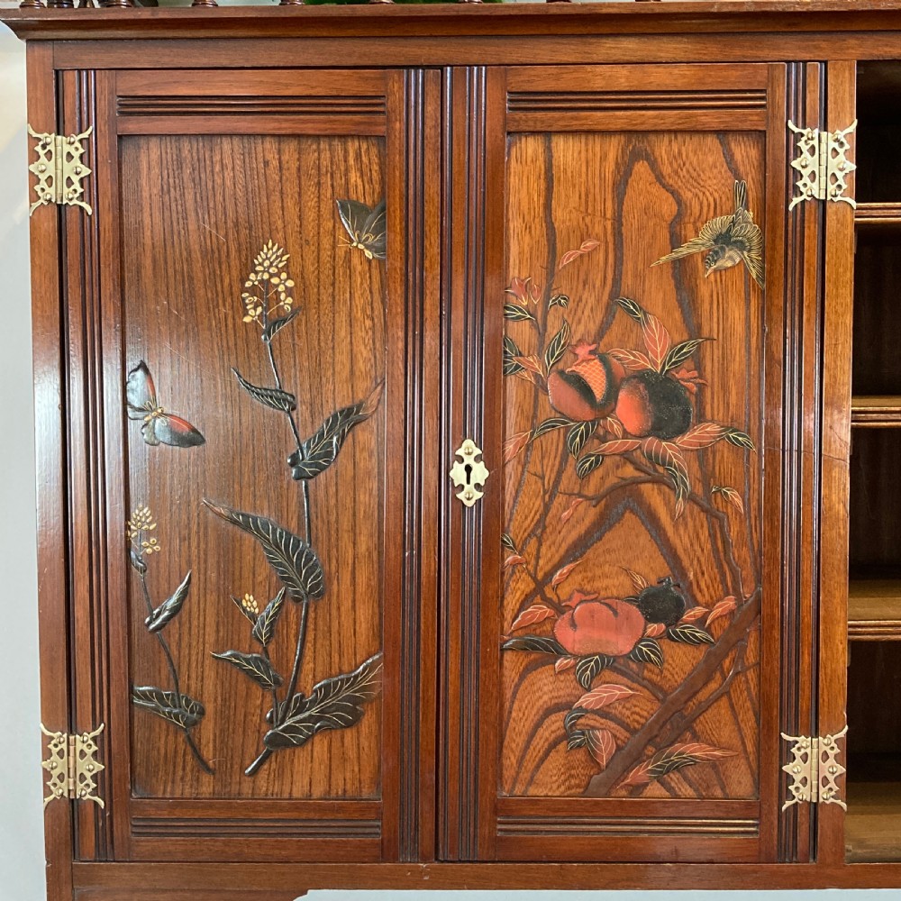 An Aesthetic Movement walnut hanging cabinet featuring three front doors decorated with carved nature motifs, a mirrored panel, exposed brass hinges, and a spindled top gallery. View II