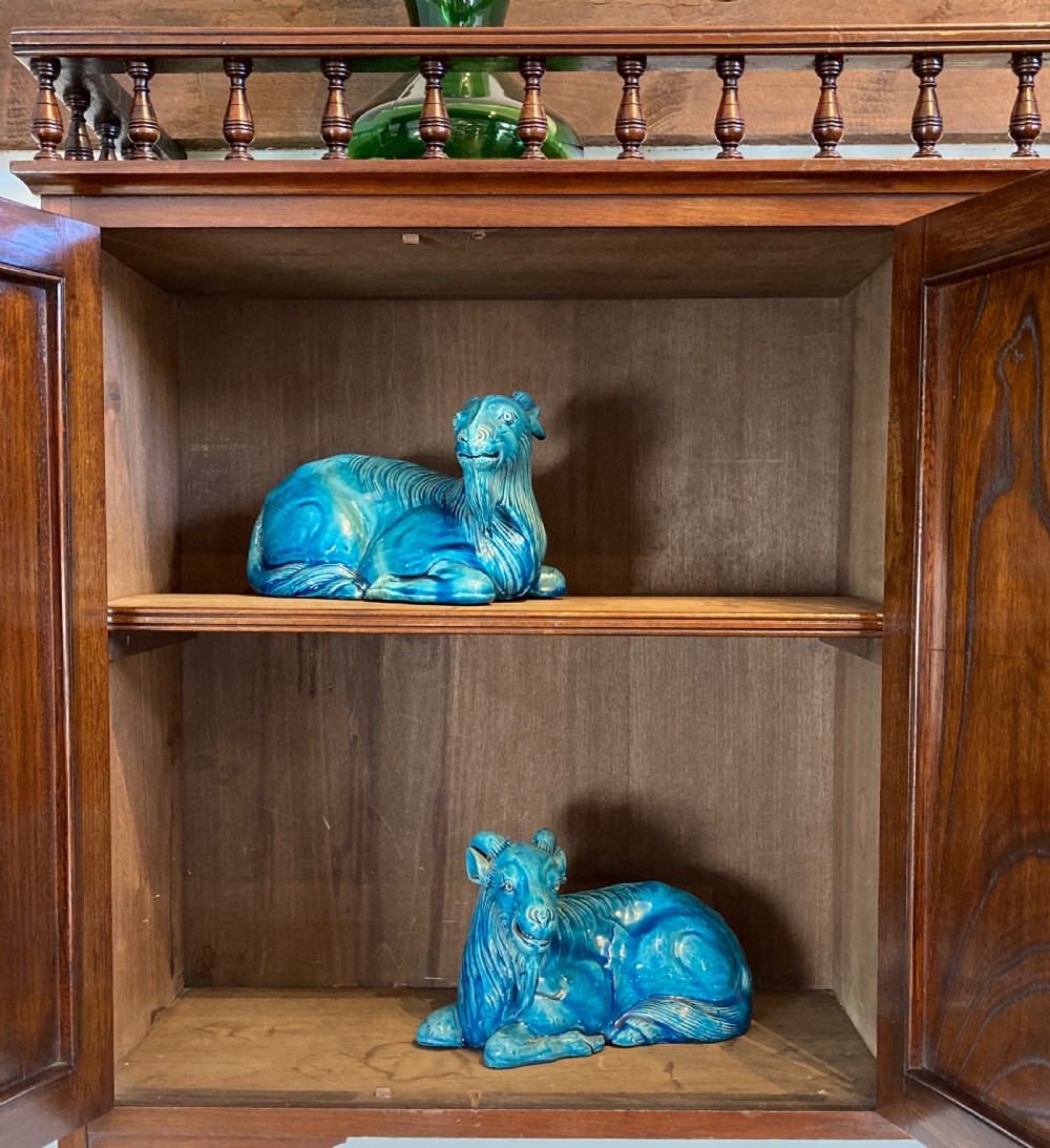 An Aesthetic Movement walnut hanging cabinet featuring three front doors decorated with carved nature motifs, a mirrored panel, exposed brass hinges, and a spindled top gallery. View VI