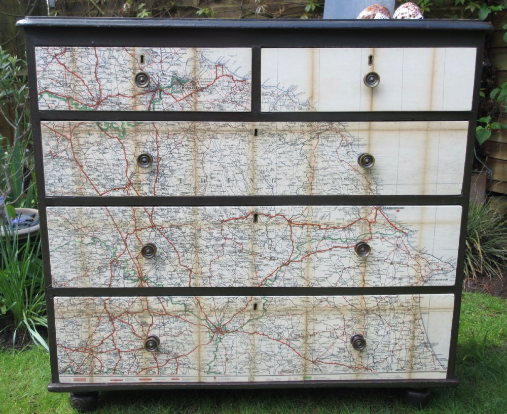 A dark painted Victorian pine chest of drawers with two short drawers over three long drawers, featuring vintage map illustrations across the drawer fronts.
