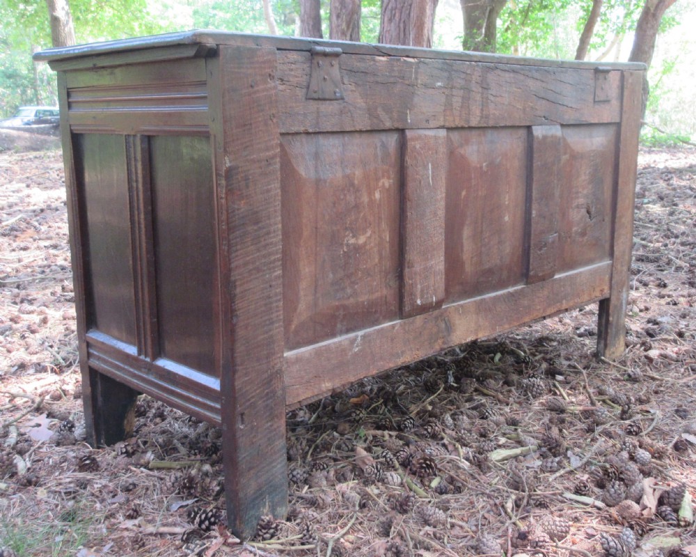 A mid-17th-century dark oak coffer featuring a flat hinged lid, triple-panelled front with split-baluster detail, and sturdy stile legs. View V