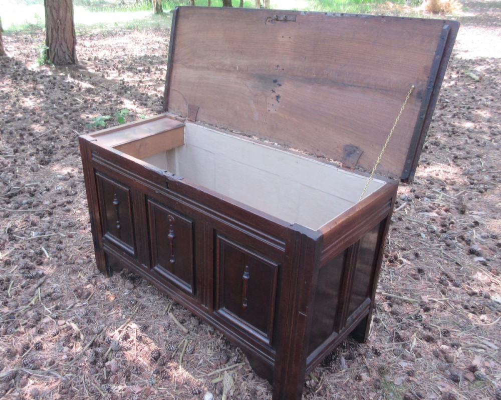 A mid-17th-century dark oak coffer featuring a flat hinged lid, triple-panelled front with split-baluster detail, and sturdy stile legs. View VI