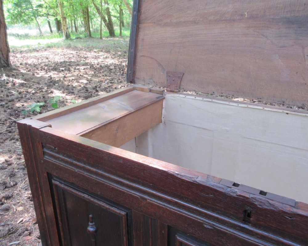 A mid-17th-century dark oak coffer featuring a flat hinged lid, triple-panelled front with split-baluster detail, and sturdy stile legs. View VII