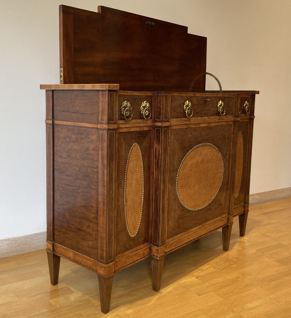 A late 18th-century George III breakfront wooden side cabinet featuring central and flanking drawers above doors decorated with oval satinwood marquetry panels and brass ring handles. View VI