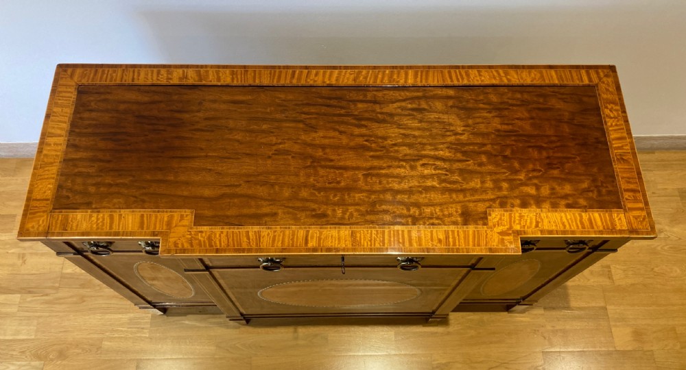 A late 18th-century George III breakfront wooden side cabinet featuring central and flanking drawers above doors decorated with oval satinwood marquetry panels and brass ring handles. View IX