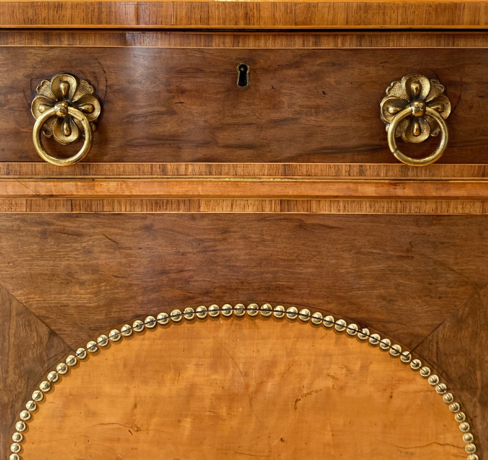 A late 18th-century George III breakfront wooden side cabinet featuring central and flanking drawers above doors decorated with oval satinwood marquetry panels and brass ring handles. View XII