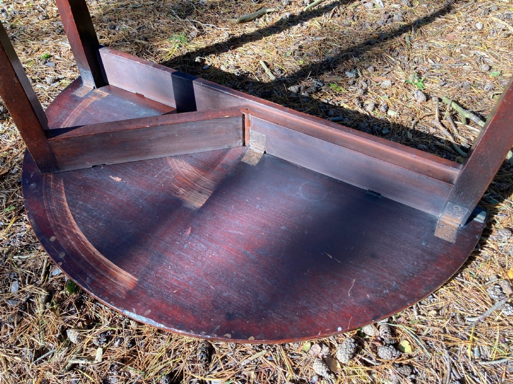 A late Georgian semi-circular mahogany folding campaign table with a polished finish and tapered legs resting outdoors. View IX