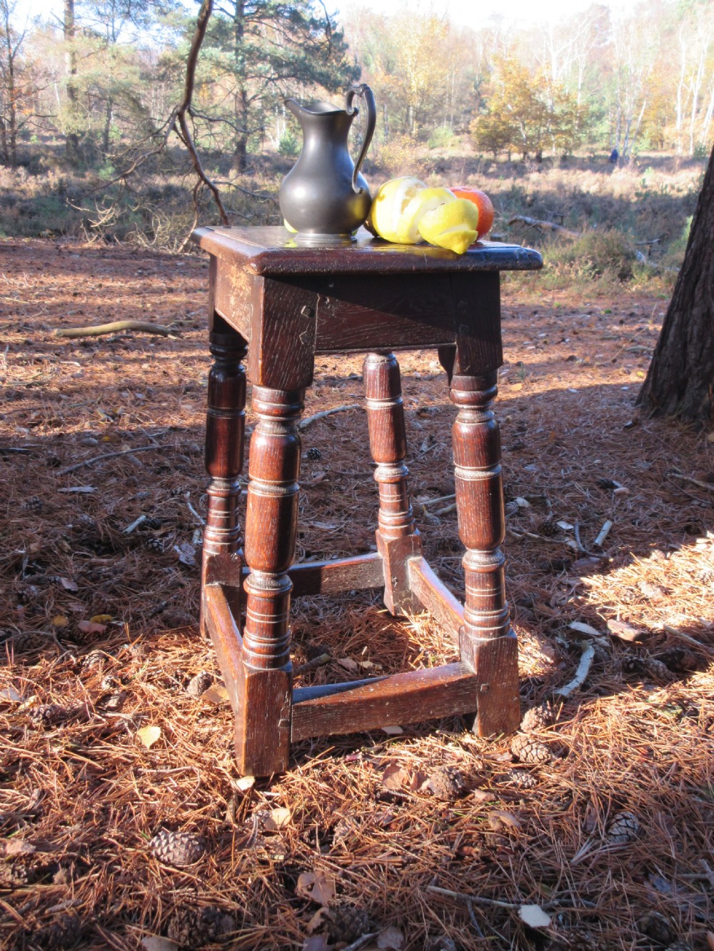 A mid-seventeenth century dark oak joint stool featuring turned legs, lower perimeter stretchers, and exposed wooden peg joinery. View III