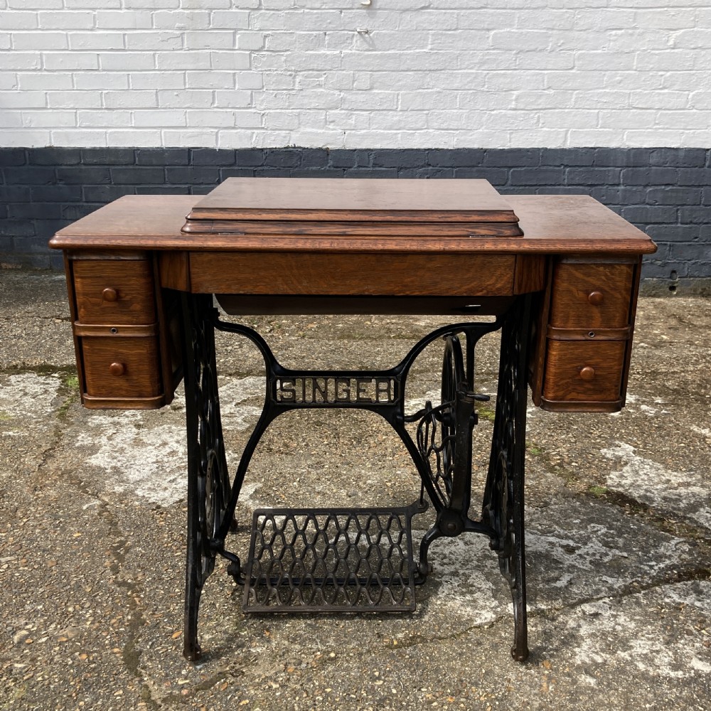 An oak-cased Singer sewing machine side table with side drawers mounted on a black cast iron treadle base.