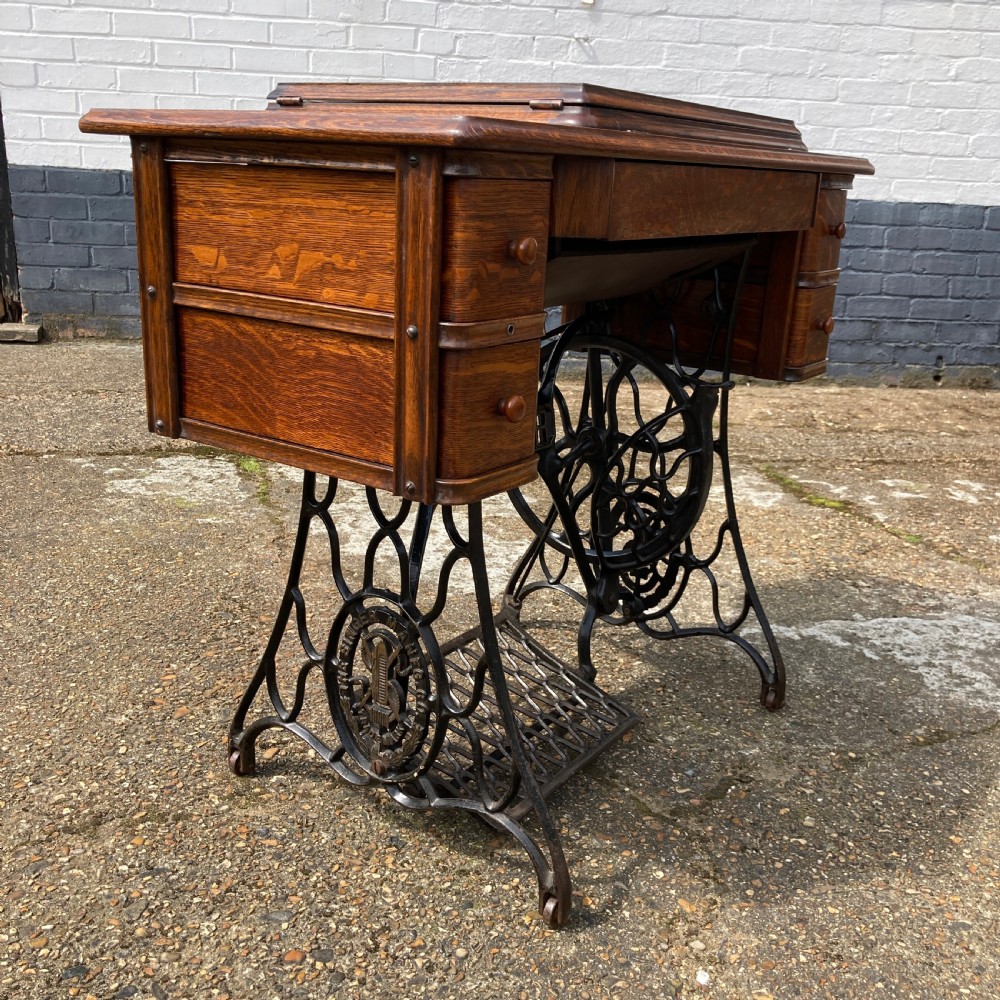 An oak-cased Singer sewing machine side table with side drawers mounted on a black cast iron treadle base. View VI