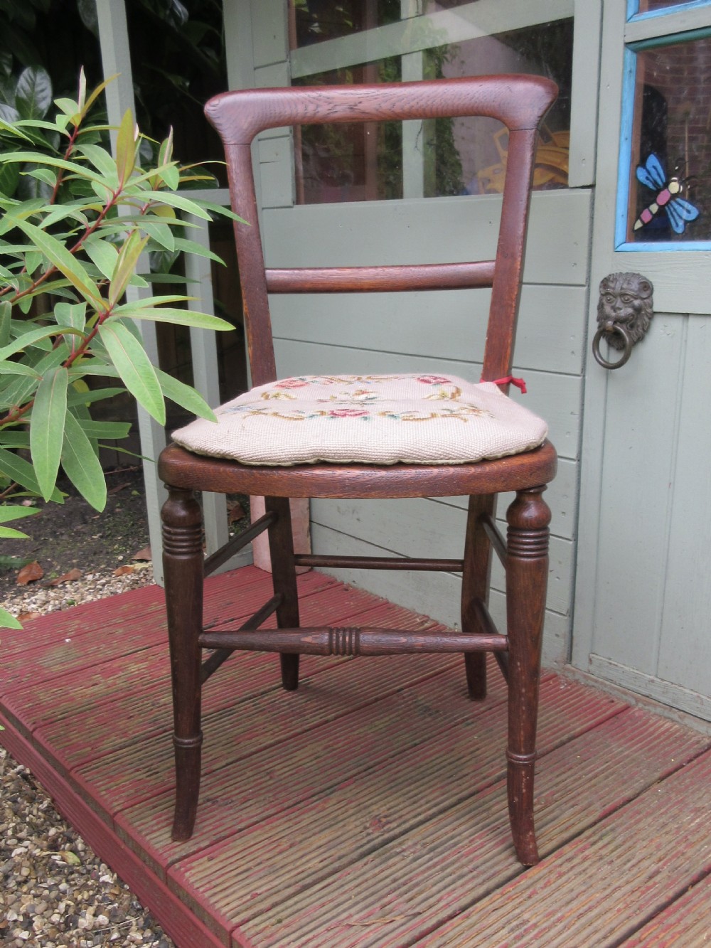 An antique dark oak side chair featuring turned front legs, a single horizontal back rail, and a floral needlepoint cushion pad.
