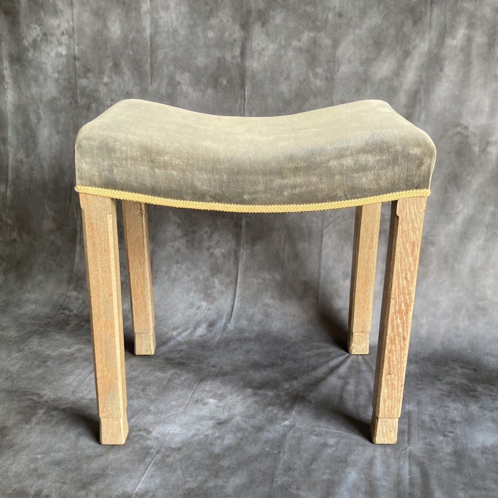 A 1937 King George VI coronation stool featuring a limed oak frame, chamfered legs, and a concave velvet seat edged with gold braid. View VI
