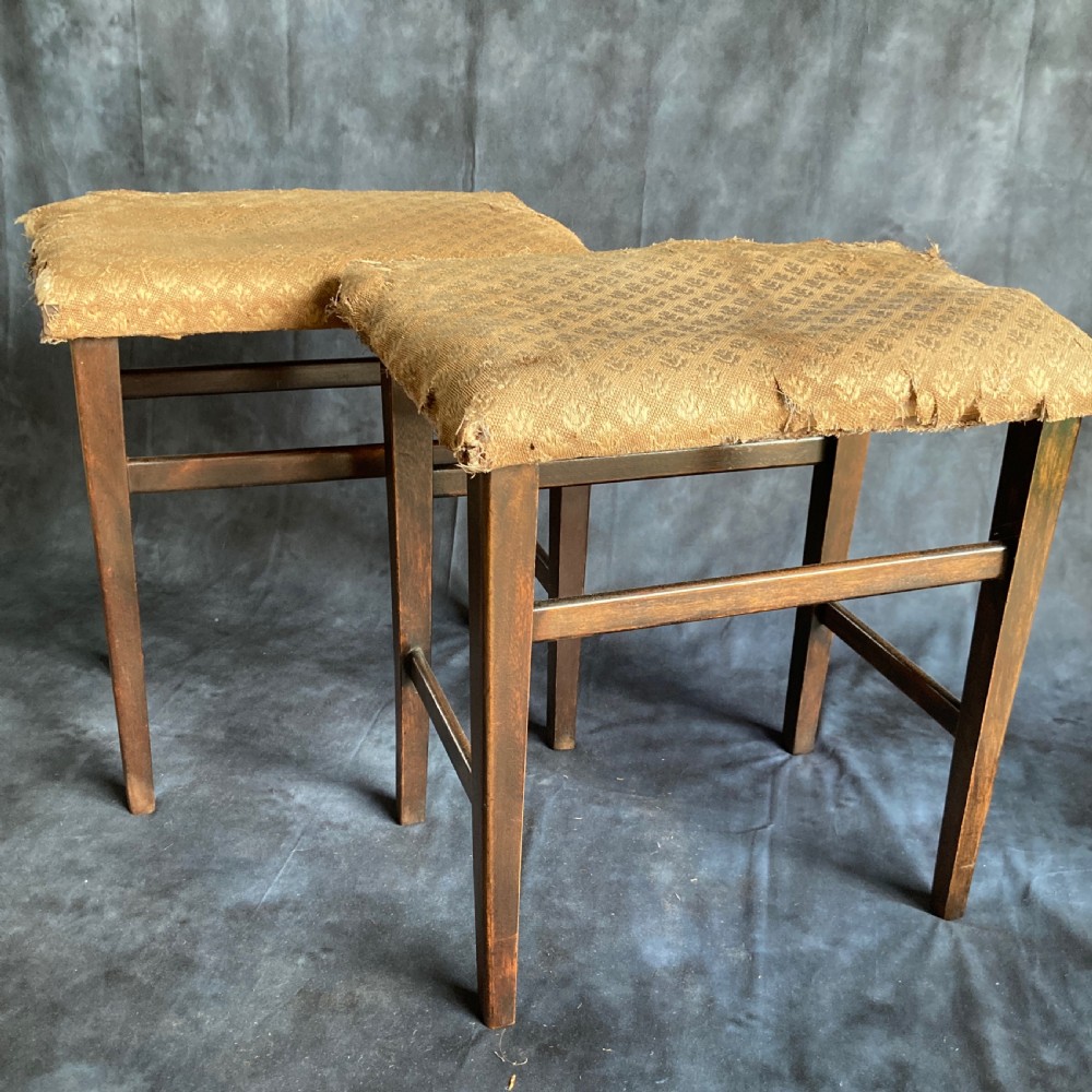 A pair of early 20th-century dark oak stools featuring patterned gold upholstery and rectangular tapered legs.