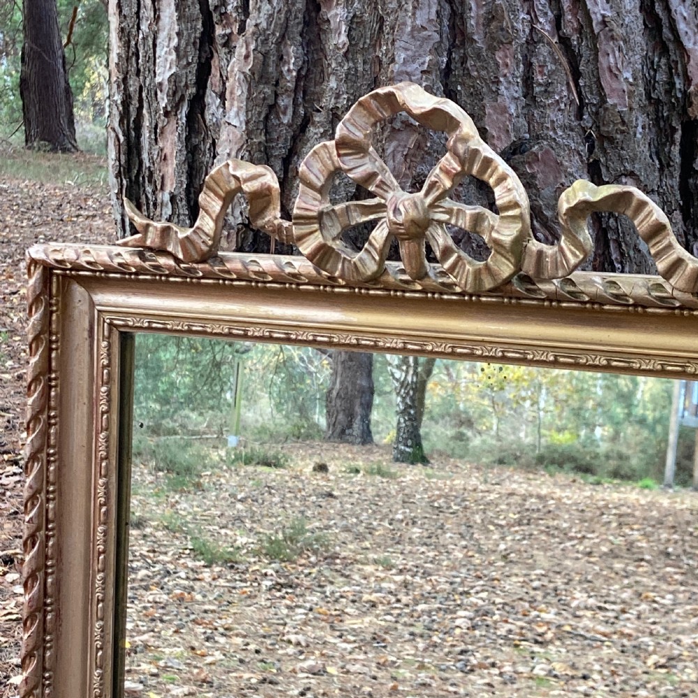 A rectangular Victorian wall mirror in a gold giltwood frame with a rope-twist inner border and a ribbon bow cresting. View II