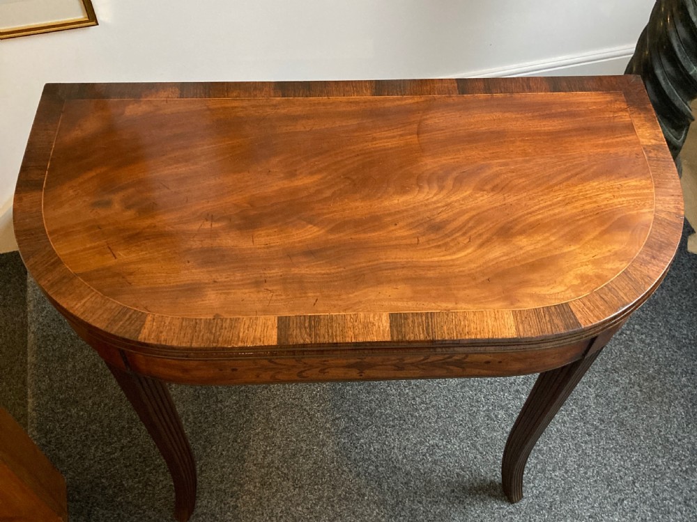 A late Georgian mahogany fold-over tea table featuring an inlaid apron and four reeded legs. View X