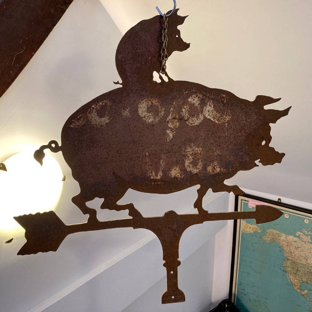 A wrought iron weather vane featuring a silhouette of a large pig with a smaller pig on its back, mounted on a directional arrow with a weathered brown patina. View III