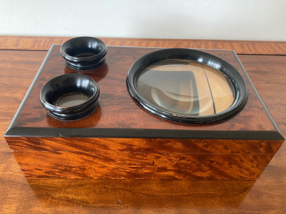 An antique Victorian hinged burr yew wood tabletop stereoscope shown open, featuring dual circular viewing lenses, a central magnifying lens, and a selection of stereoview cards. View II
