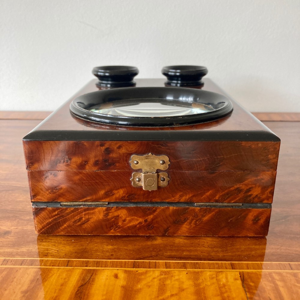 An antique Victorian hinged burr yew wood tabletop stereoscope shown open, featuring dual circular viewing lenses, a central magnifying lens, and a selection of stereoview cards. View IX