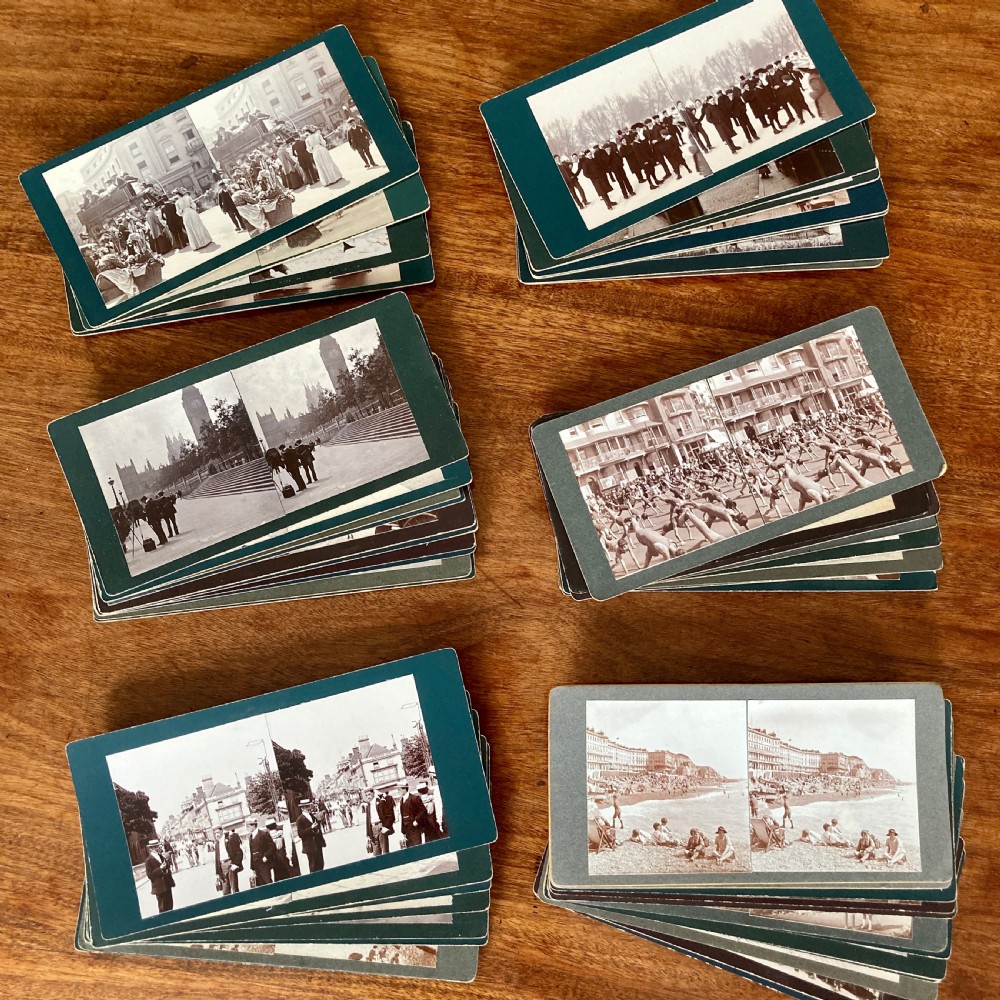 An antique Victorian hinged burr yew wood tabletop stereoscope shown open, featuring dual circular viewing lenses, a central magnifying lens, and a selection of stereoview cards. View XI