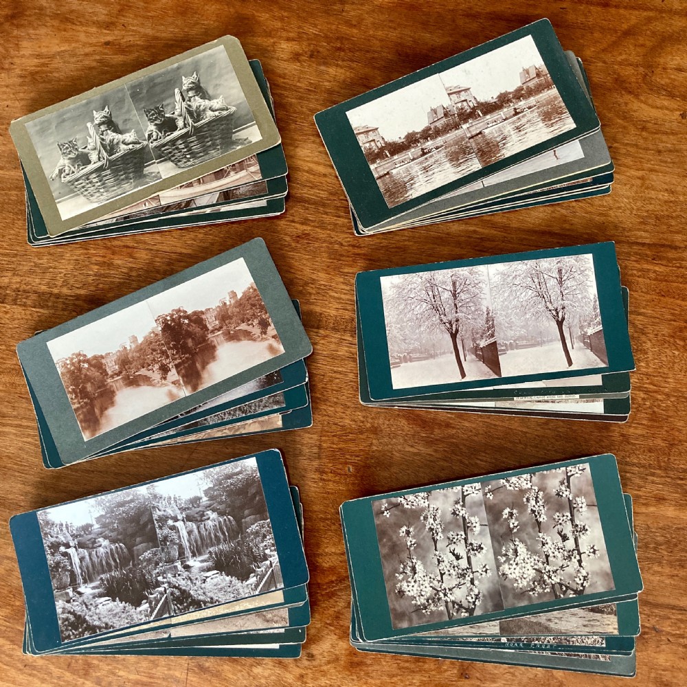 An antique Victorian hinged burr yew wood tabletop stereoscope shown open, featuring dual circular viewing lenses, a central magnifying lens, and a selection of stereoview cards. View XII