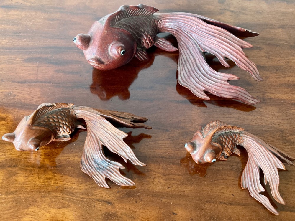 Three 19th-century Oriental carved wooden goldfish figures with detailed scales, flowing fins, and inset glass eyes displayed on a polished surface.