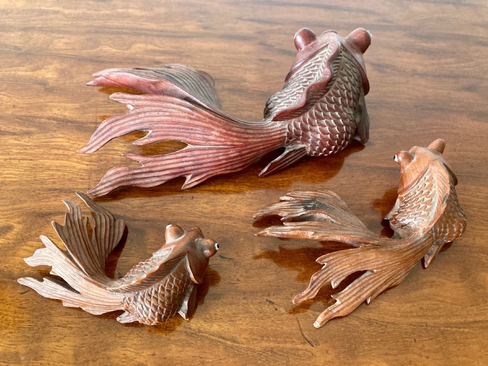 Three 19th-century Oriental carved wooden goldfish figures with detailed scales, flowing fins, and inset glass eyes displayed on a polished surface. View V