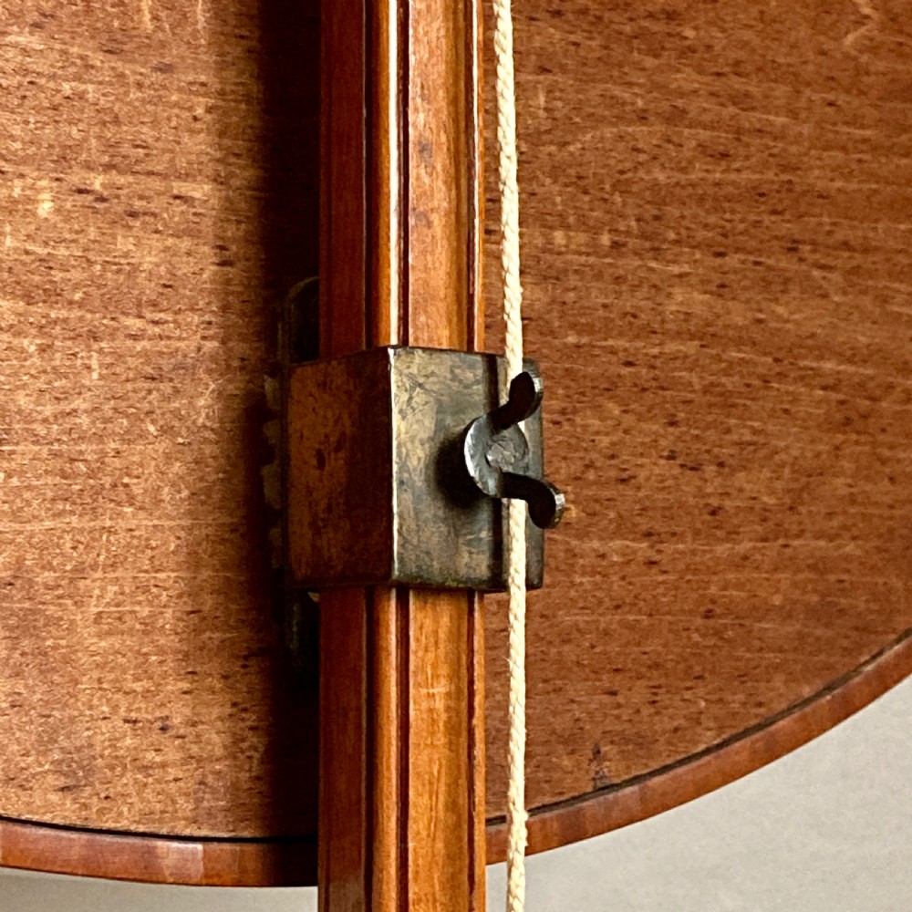 An oval mahogany fire screen containing an 18th-century silk needlework scene of pastoral figures, mounted on a central wooden pole. View IX