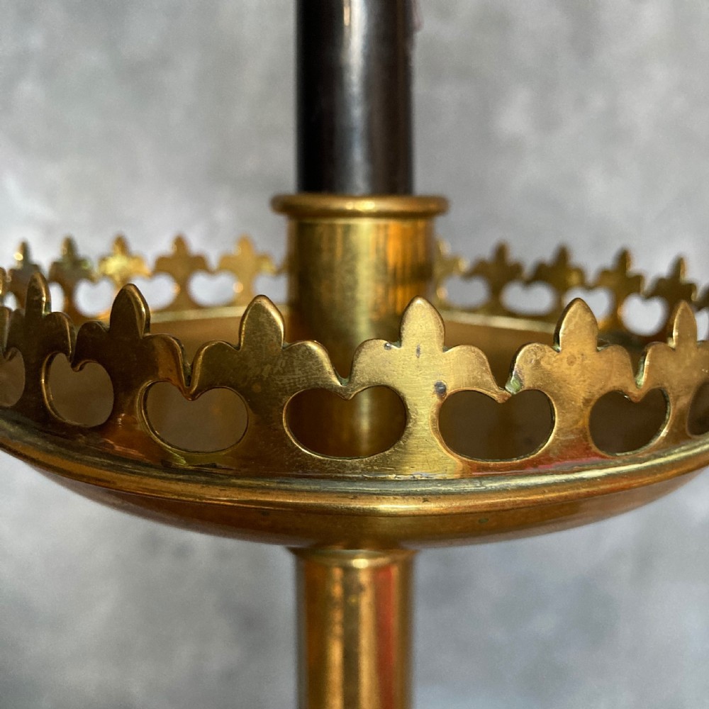 A pair of tall Victorian Gothic Revival cast brass candlesticks featuring pierced crenellated drip pans, knopped stems, and stylized paw feet. View II