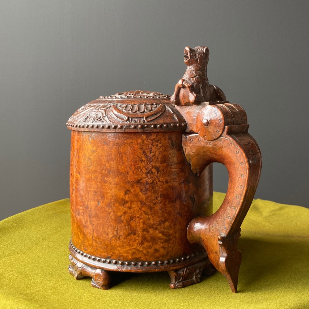 An 18th-century Norwegian carved wooden peg tankard featuring a lion thumbpiece, domed relief-carved lid, and carved lion feet in a warm brown finish.