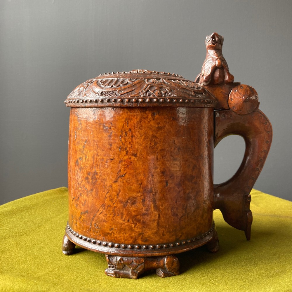 An 18th-century Norwegian carved wooden peg tankard featuring a lion thumbpiece, domed relief-carved lid, and carved lion feet in a warm brown finish. View II