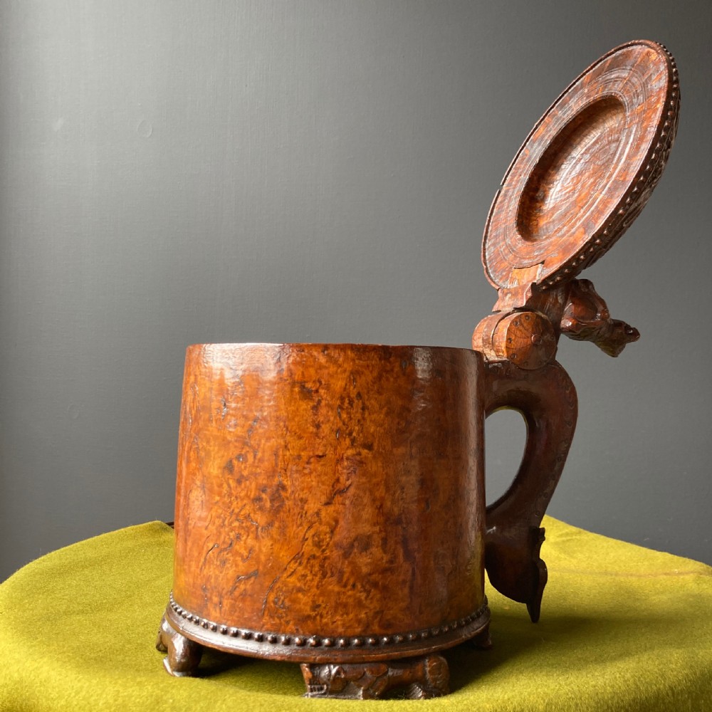 An 18th-century Norwegian carved wooden peg tankard featuring a lion thumbpiece, domed relief-carved lid, and carved lion feet in a warm brown finish. View V