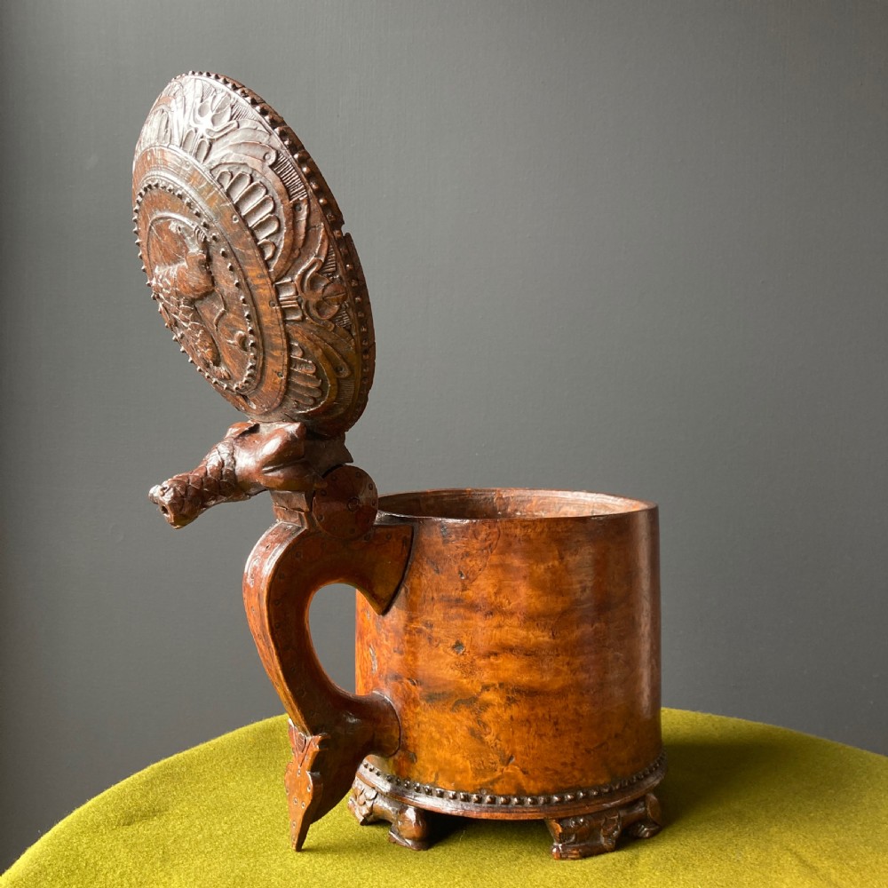 An 18th-century Norwegian carved wooden peg tankard featuring a lion thumbpiece, domed relief-carved lid, and carved lion feet in a warm brown finish. View VI