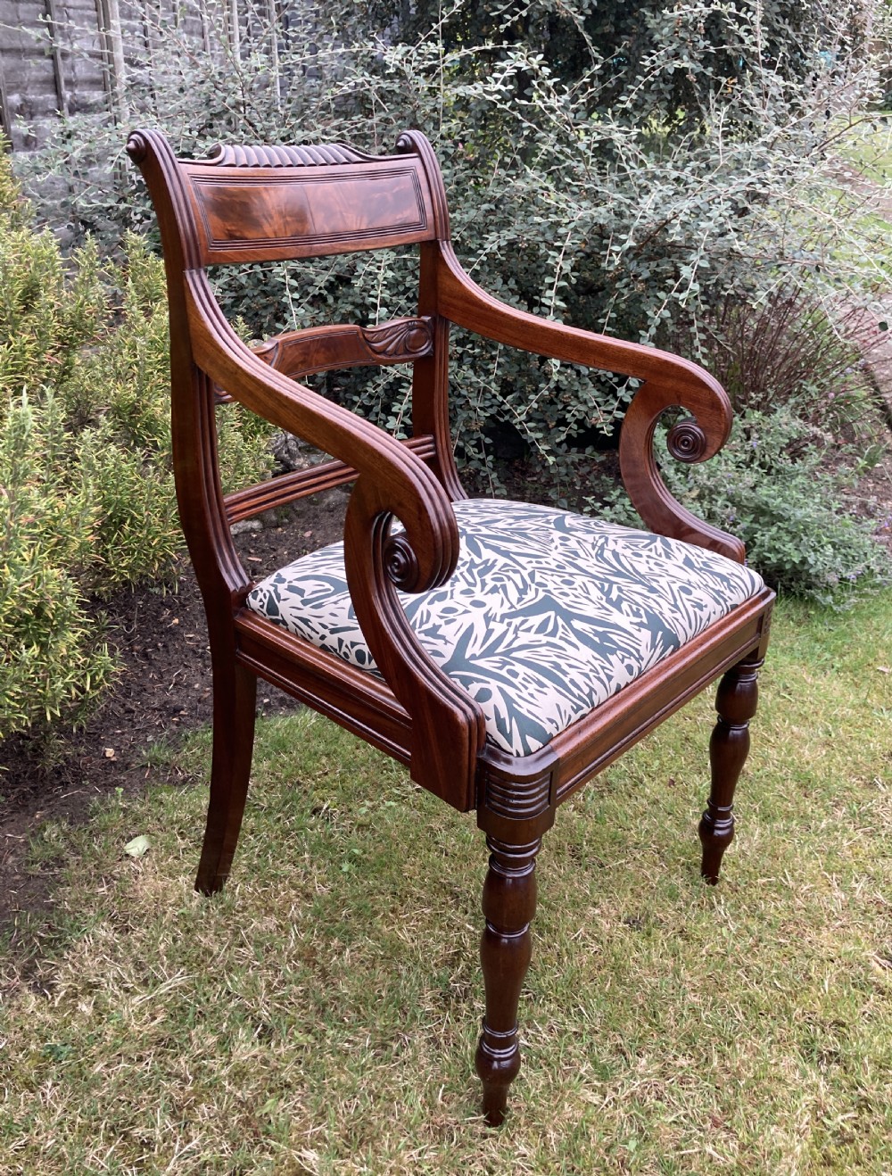A George III mahogany desk armchair featuring reeded arms, a tablet top rail with flame mahogany veneer, and a patterned upholstered seat. View X