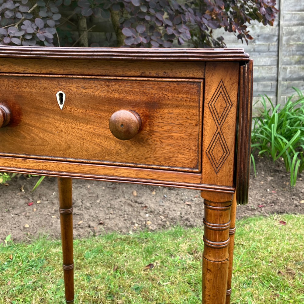 A late Georgian mahogany work table featuring twin drop leaves, a single drawer with wooden knobs, inlaid diamond details, and turned legs on brass castors. View II