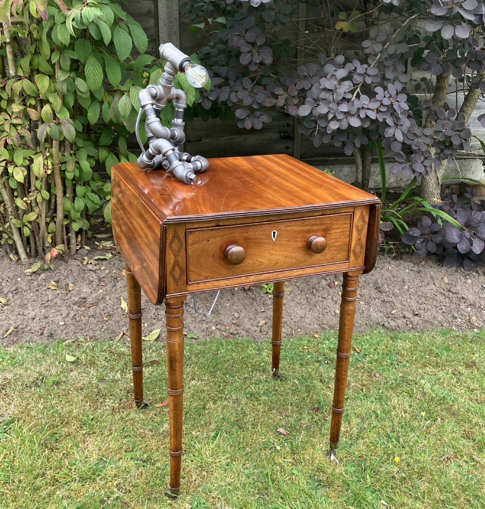 A late Georgian mahogany work table featuring twin drop leaves, a single drawer with wooden knobs, inlaid diamond details, and turned legs on brass castors. View III