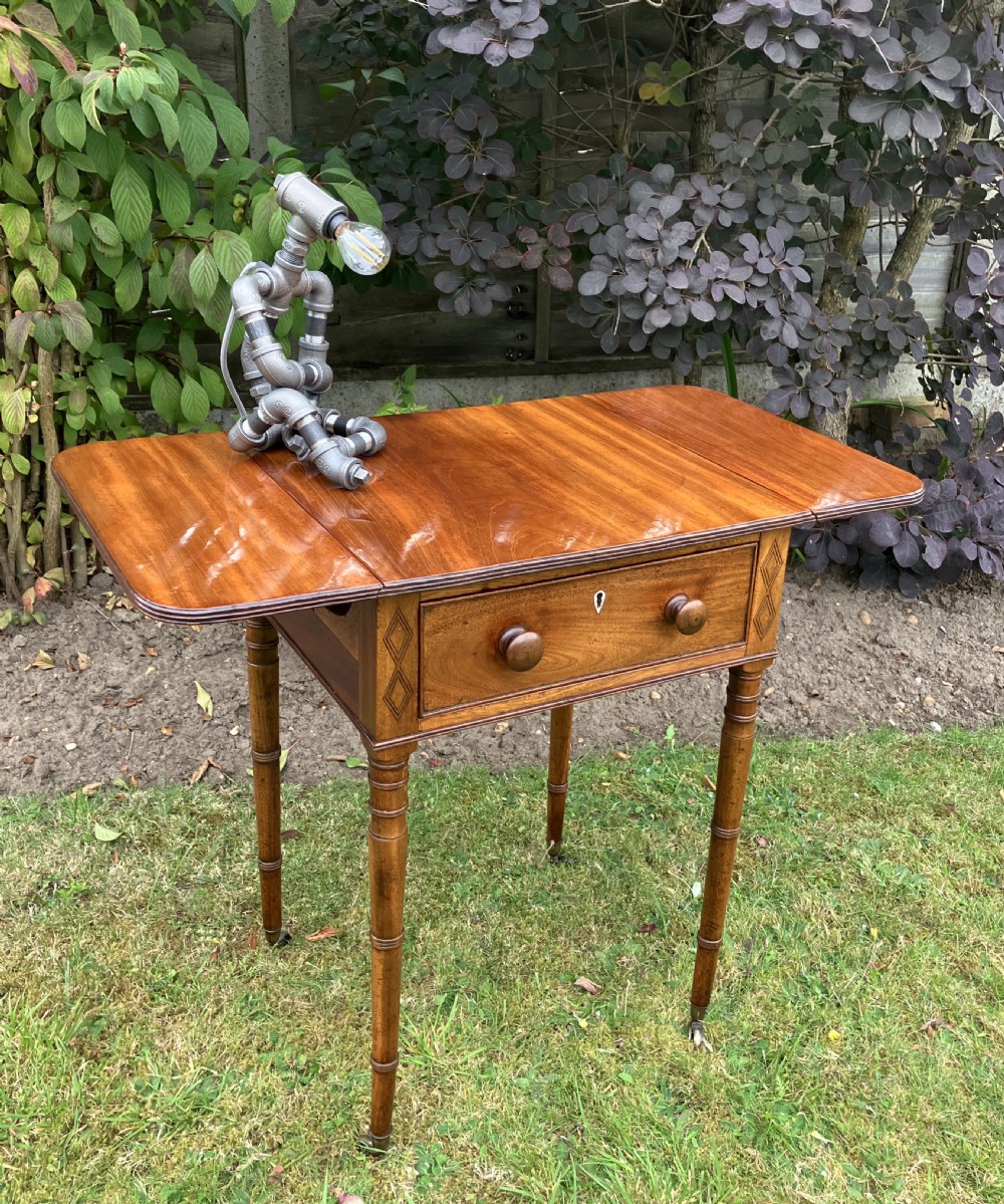 A late Georgian mahogany work table featuring twin drop leaves, a single drawer with wooden knobs, inlaid diamond details, and turned legs on brass castors. View XI