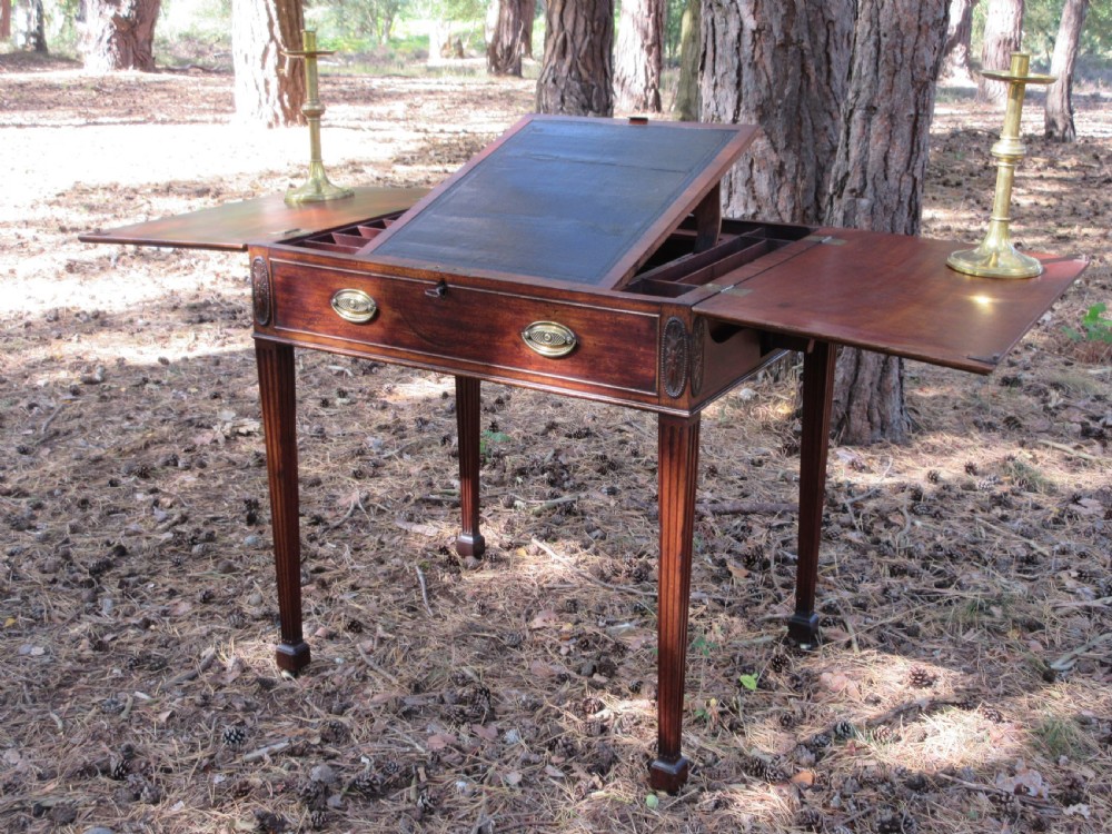 A George III mahogany estate rent table featuring an adjustable leather writing slope, document compartments, side flap extensions, and fluted legs.