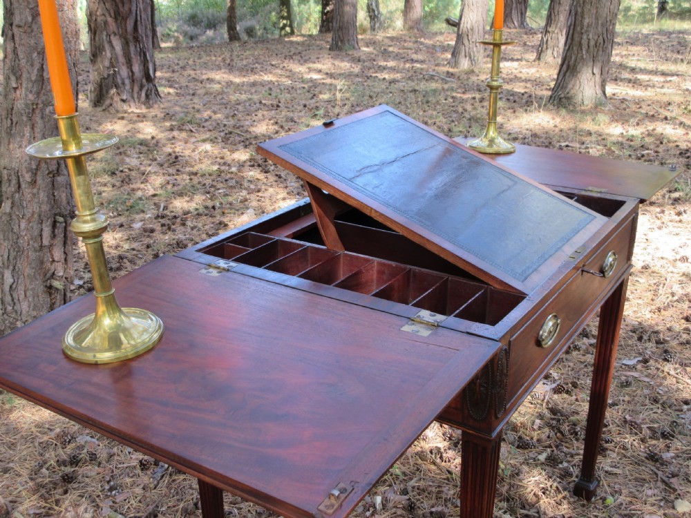 A George III mahogany estate rent table featuring an adjustable leather writing slope, document compartments, side flap extensions, and fluted legs. View III