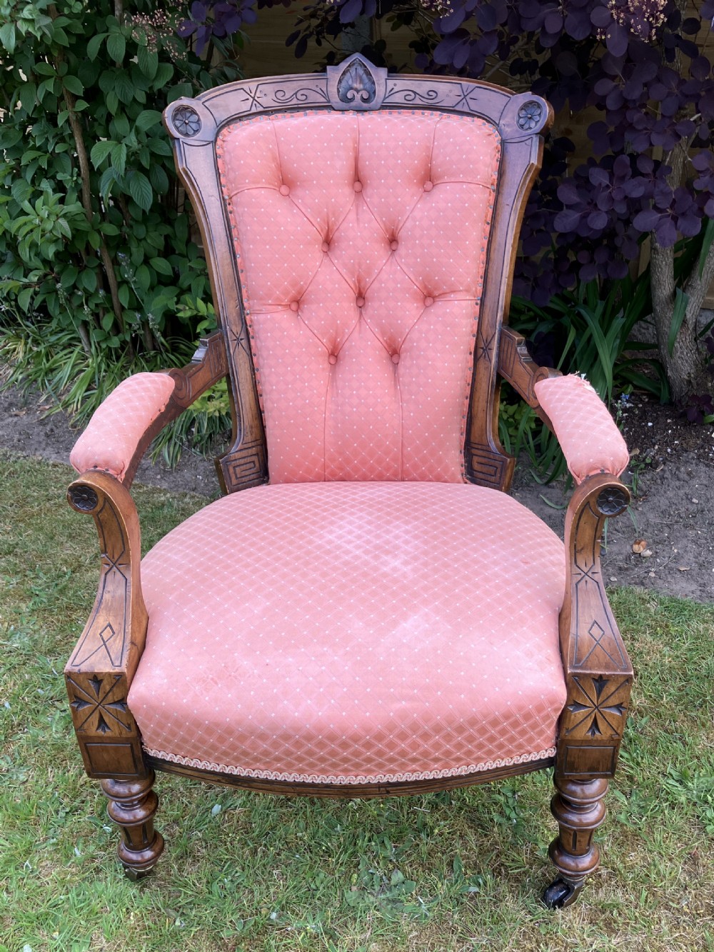 A Victorian walnut open armchair featuring pink patterned button-backed upholstery, a carved wood frame, and turned legs on castors.