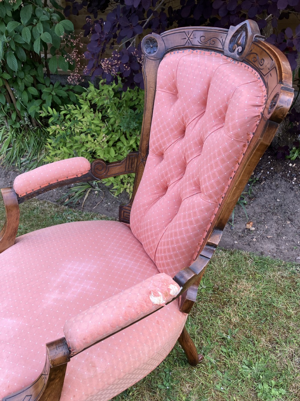 A Victorian walnut open armchair featuring pink patterned button-backed upholstery, a carved wood frame, and turned legs on castors. View V