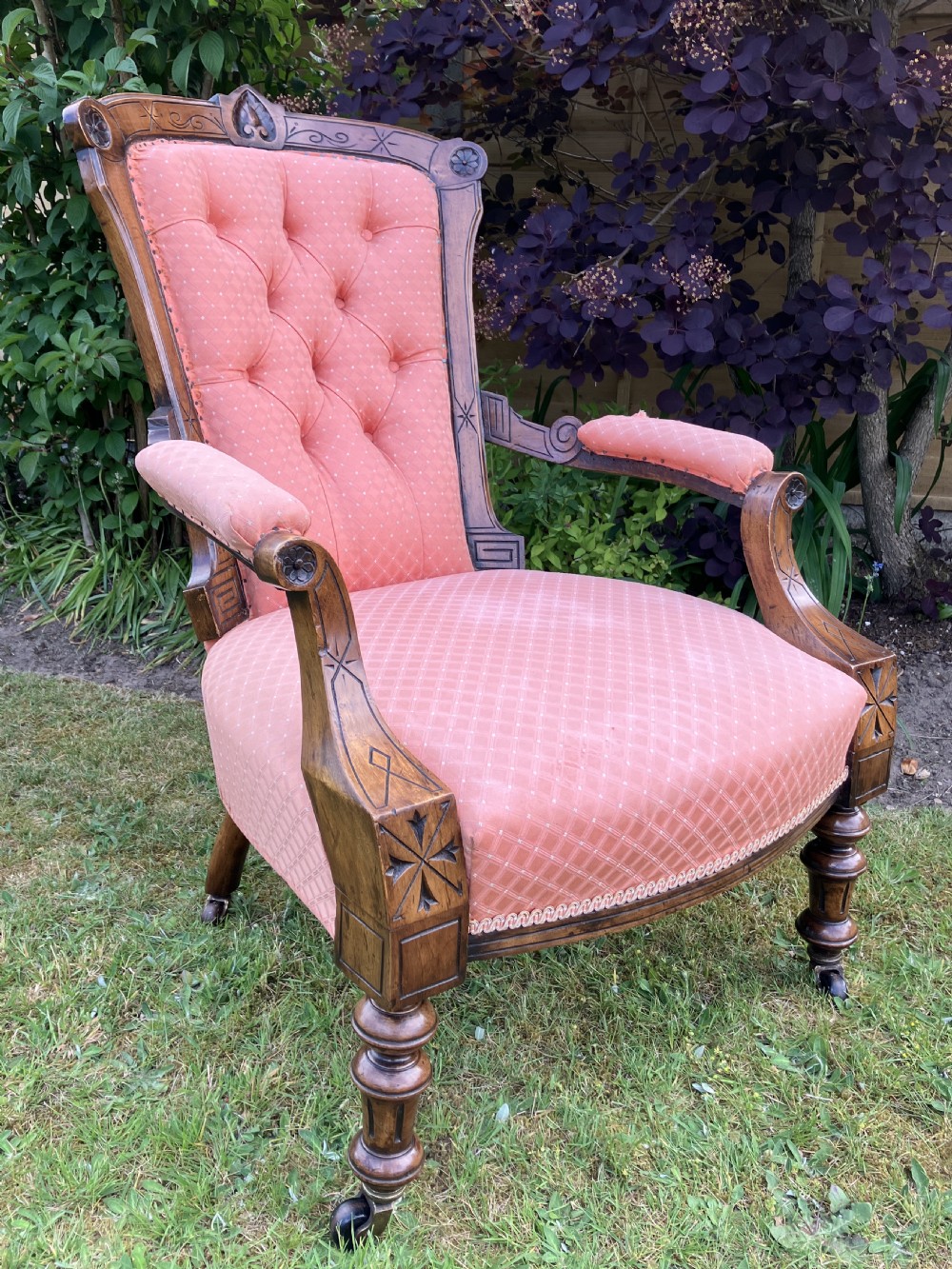 A Victorian walnut open armchair featuring pink patterned button-backed upholstery, a carved wood frame, and turned legs on castors. View VIII