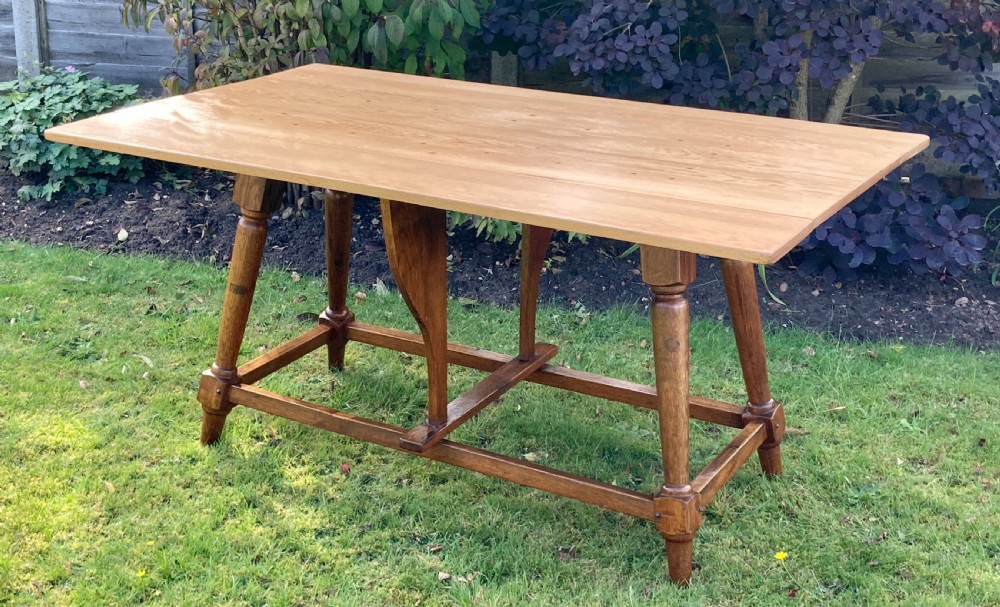 A solid oak Arts and Crafts refectory dining table featuring drop-leaf extensions, turned legs, and an H-stretcher base. View II