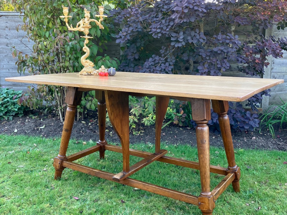 A solid oak Arts and Crafts refectory dining table featuring drop-leaf extensions, turned legs, and an H-stretcher base.