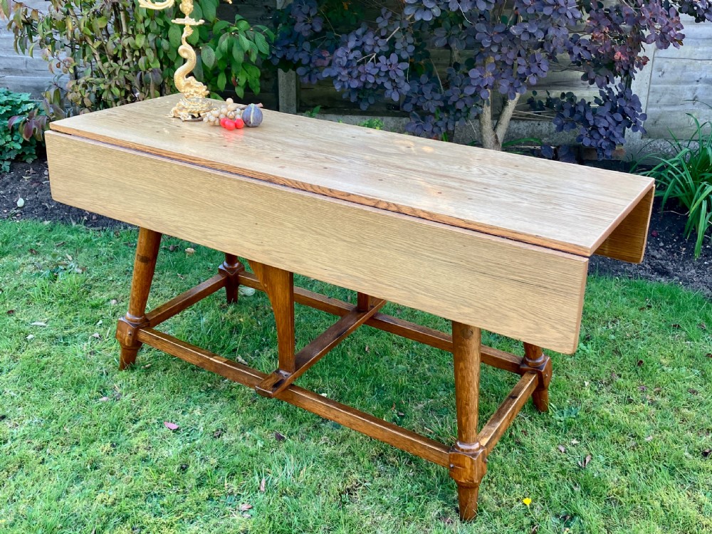 A solid oak Arts and Crafts refectory dining table featuring drop-leaf extensions, turned legs, and an H-stretcher base. View III