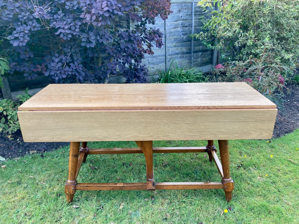 A solid oak Arts and Crafts refectory dining table featuring drop-leaf extensions, turned legs, and an H-stretcher base. View VII