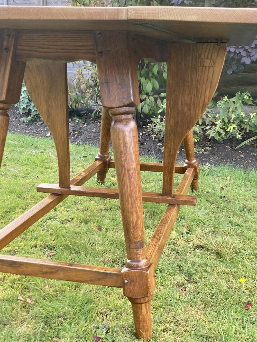 A solid oak Arts and Crafts refectory dining table featuring drop-leaf extensions, turned legs, and an H-stretcher base. View X