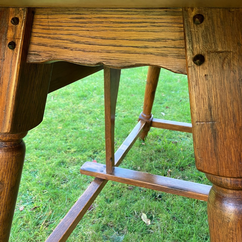 A solid oak Arts and Crafts refectory dining table featuring drop-leaf extensions, turned legs, and an H-stretcher base. View XI