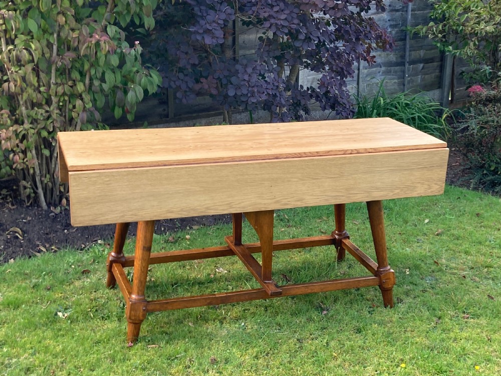 A solid oak Arts and Crafts refectory dining table featuring drop-leaf extensions, turned legs, and an H-stretcher base. View XIII